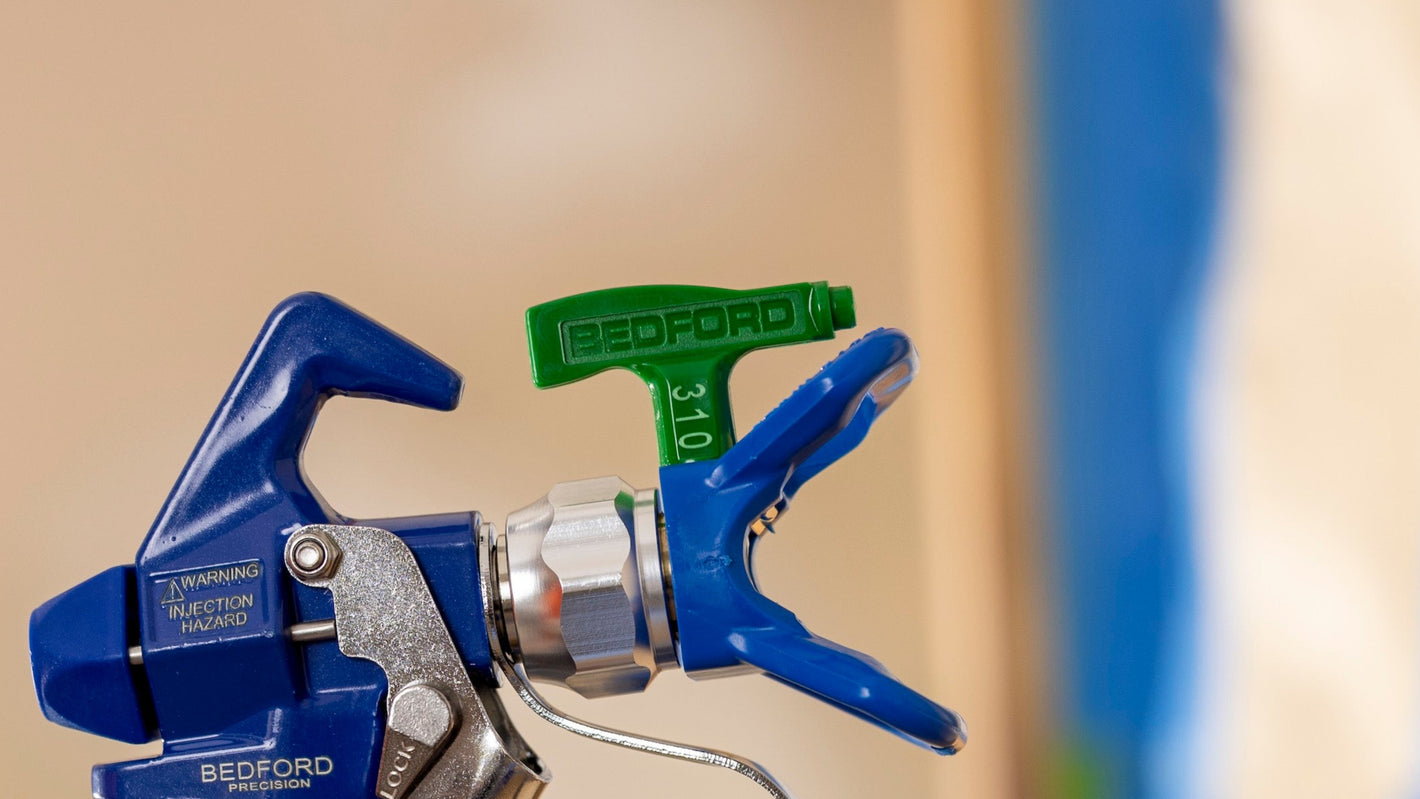 Hand holding a spray gun with a blurred background of a painting.