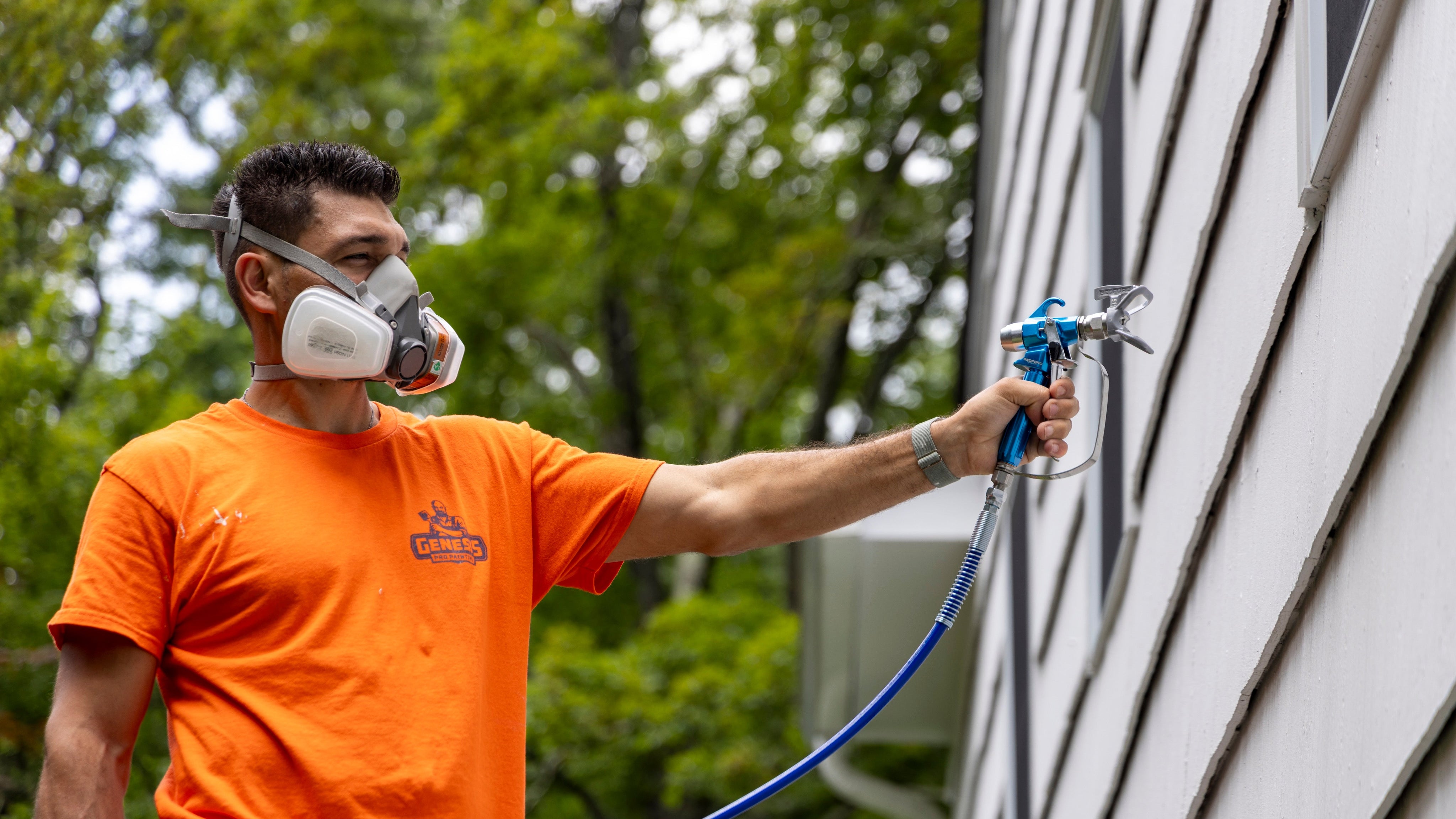 Person in orange shirt using a paint sprayer on a building exterior.